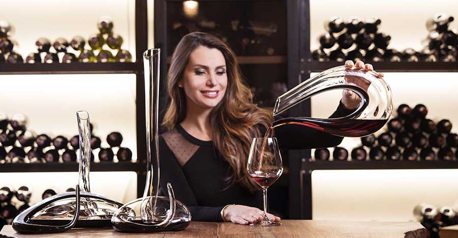 Woman pouring red wine from a Riedel crystal decanter into a wine glass