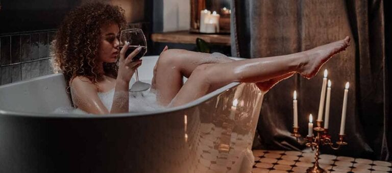 Woman in bathtub drinking red wine and showing legs