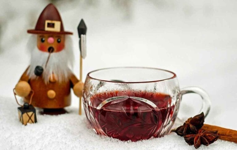 Glass of mulled wine next to Christmas doll and cinnamon stick