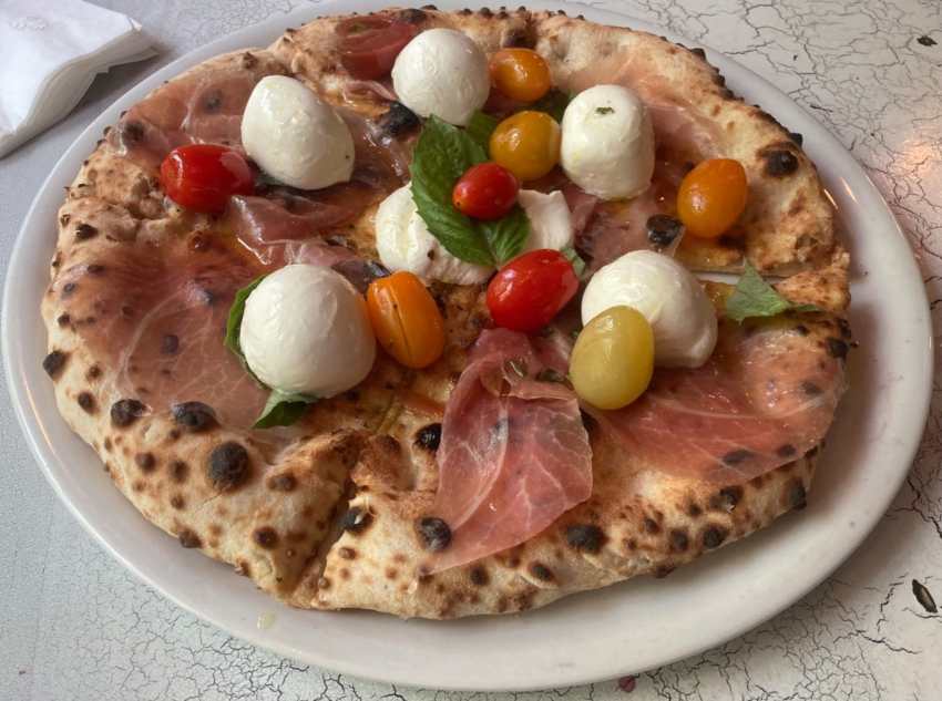 Summer pizza with mozzarella, prosciutto, whole grape tomatoes, basil, and extra virgin olive oil