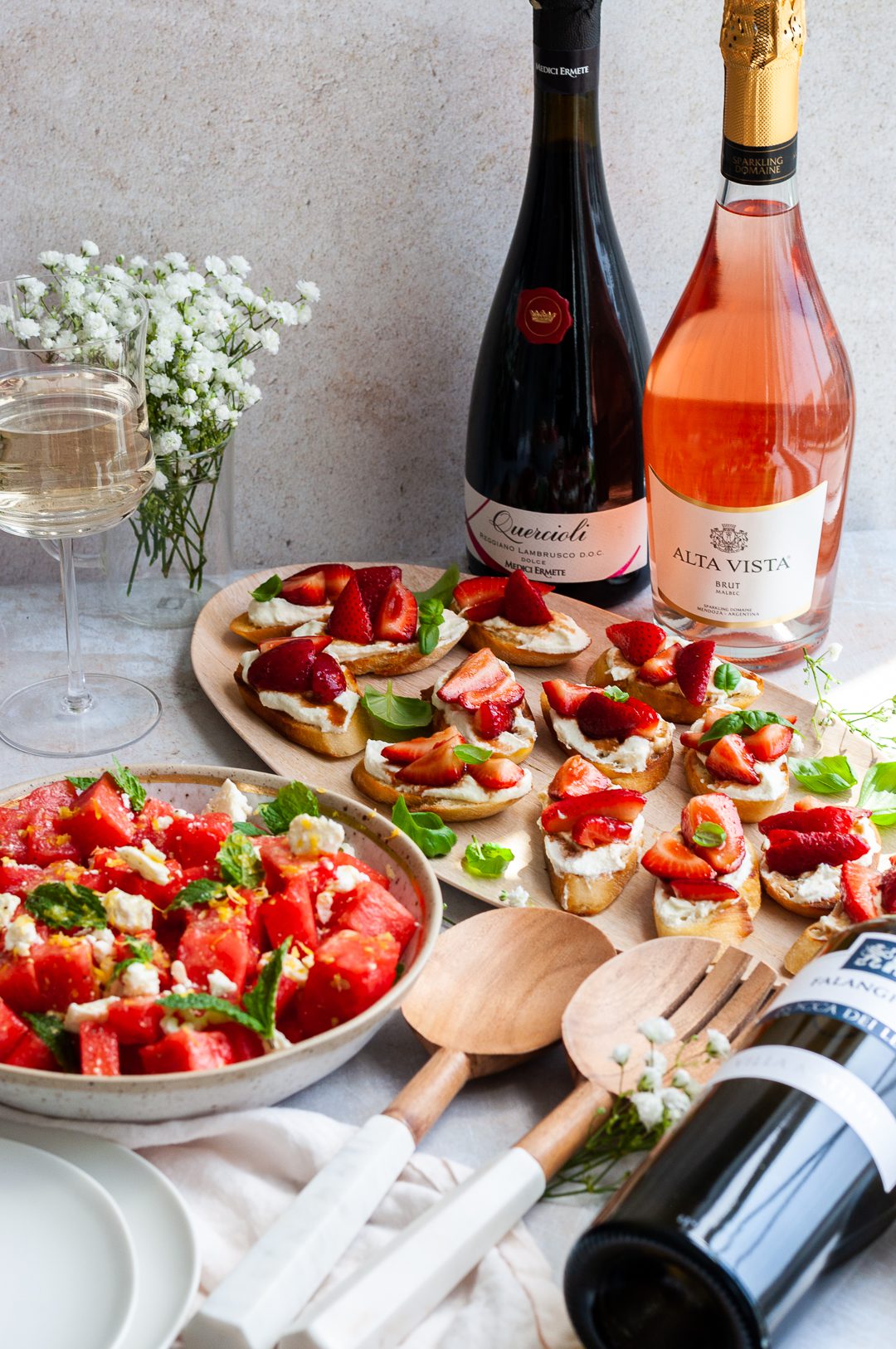 Red and rose sparkling wine bottles next to summer salads