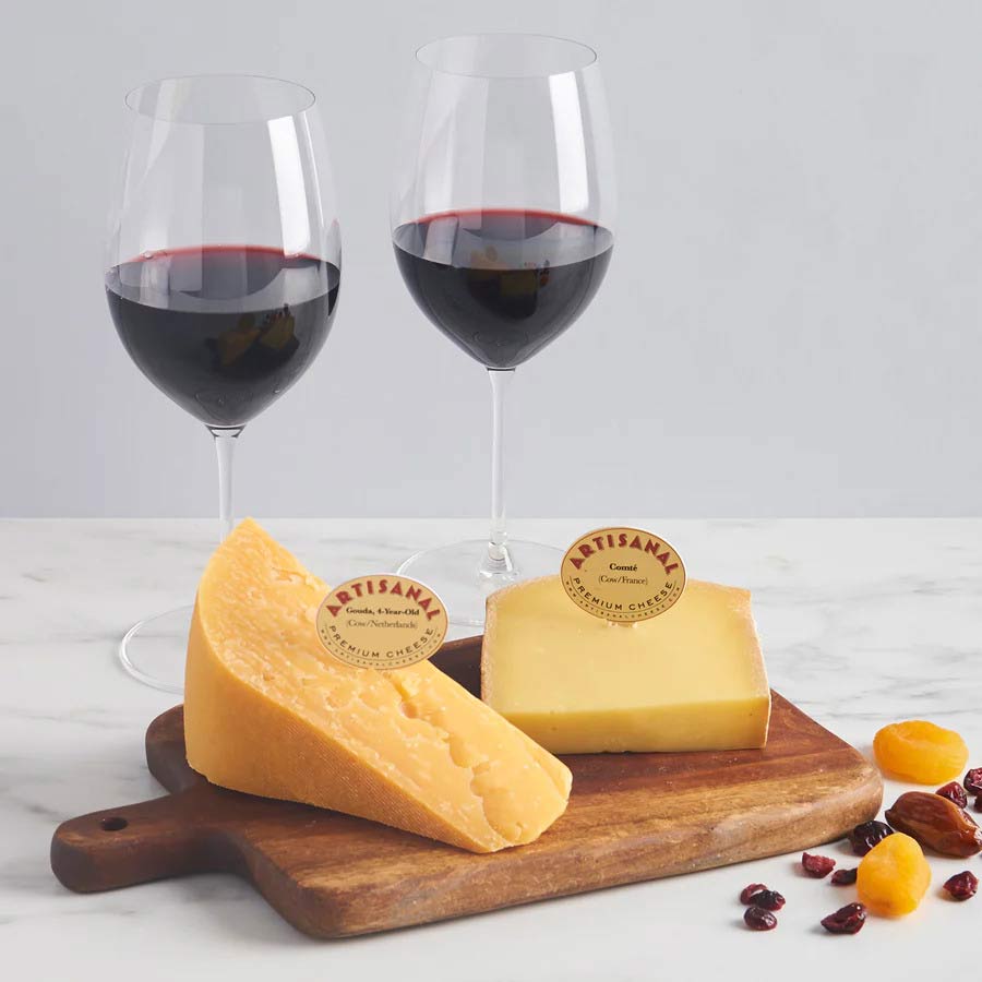 Comte and Gouda Artisanal cheeses on a cheese board with two glasses of red wine