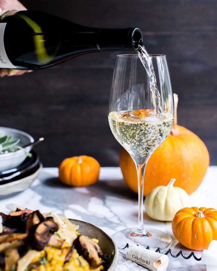 Pouring Chardonnay wine around pumpkins and risotto